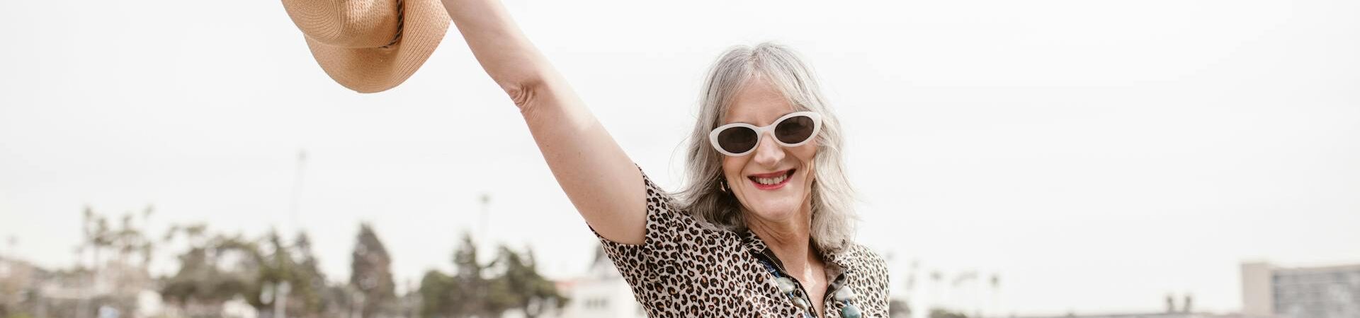 Kobieta trzymająca kapelusz, uśmiechając się na tle plaży
