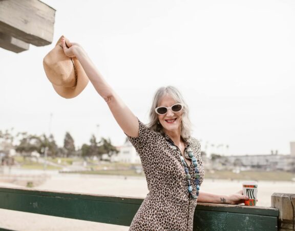 Kobieta trzymająca kapelusz, uśmiechając się na tle plaży