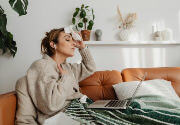 Kobieta z chusteczką na czole, siedząca na kanapie, odczuwająca uderzenia gorąca