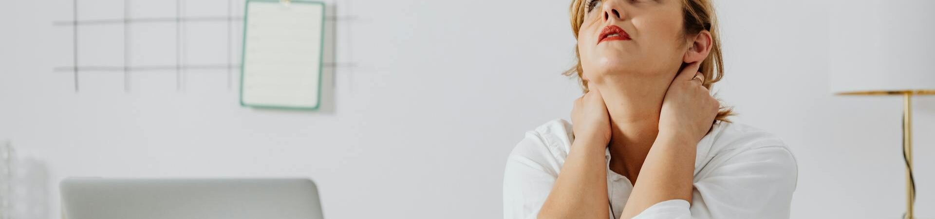 Kobieta siedząca przy biurku, z rękami na szyi, patrząca w górę, z użytymi chusteczkami obok laptopa