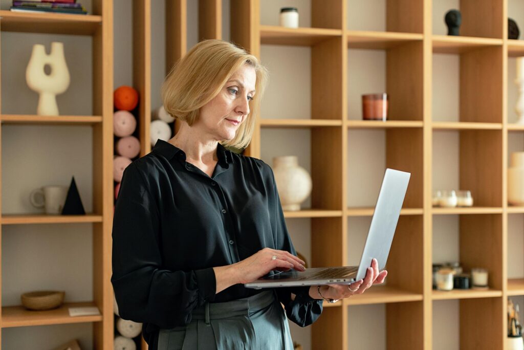Kobieta trzymaj&Auml;ca laptopa, patrz&Auml;ca na ekran, w tle rega&Aring; z dekoracjami