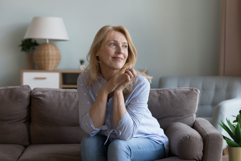 Kobieta siedzi na kanapie, opierajÄ…c dÅ‚onie o podbrÃ³dek.