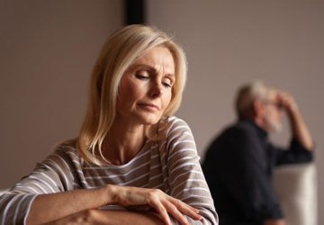 Starsza para w konflikcie, siedząca z dala od siebie, wyraźnie zmartwiona.