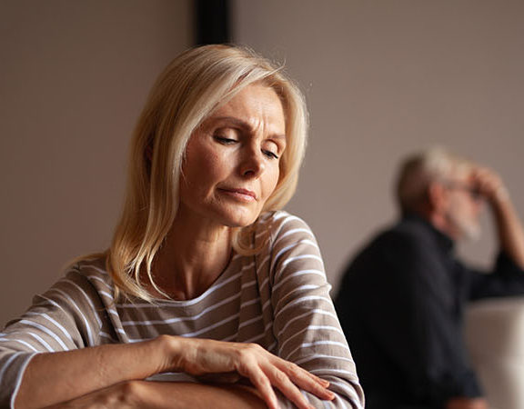 Starsza para w konflikcie, siedząca z dala od siebie, wyraźnie zmartwiona.