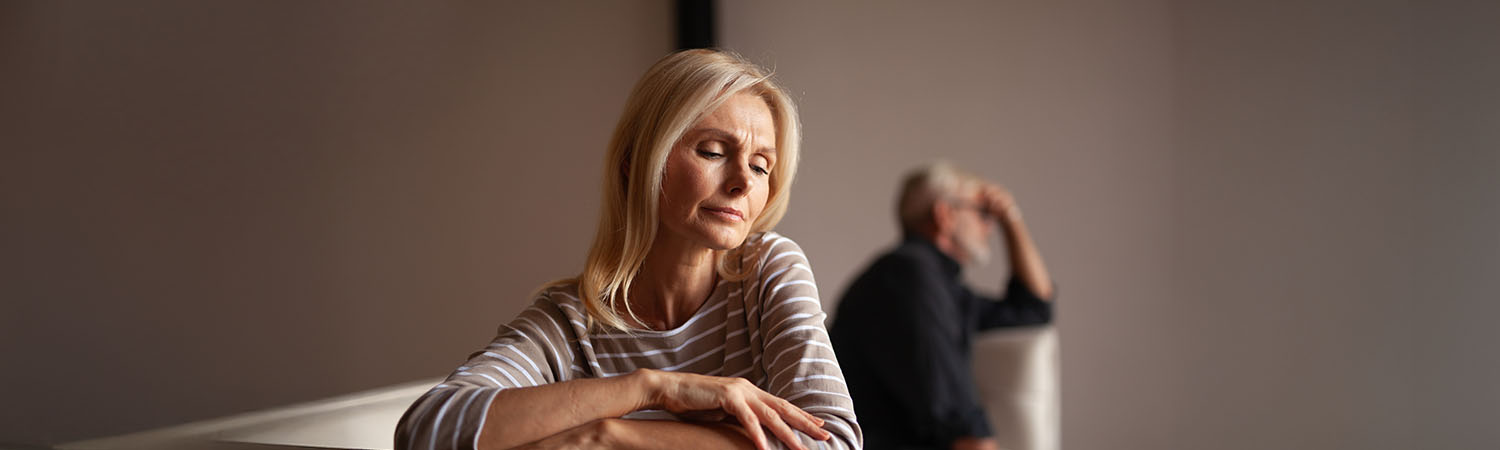 Starsza para w konflikcie, siedząca z dala od siebie, wyraźnie zmartwiona.