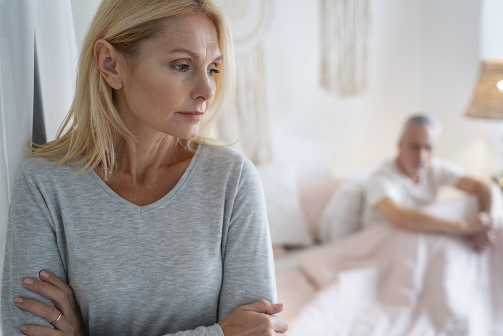 Kobieta patrzÄ
ca z zamyÅleniem, z mÄżem leżÄ
cym w tle w Åóżku.