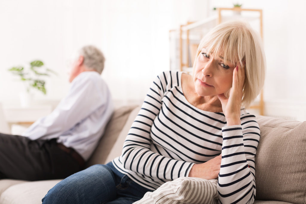 Kobieta siedzÄ
ca na kanapie z wyraźnym zmartwieniem na twarzy, a z tyÅu siedzi odwrócony plecami mÄżczyzna.