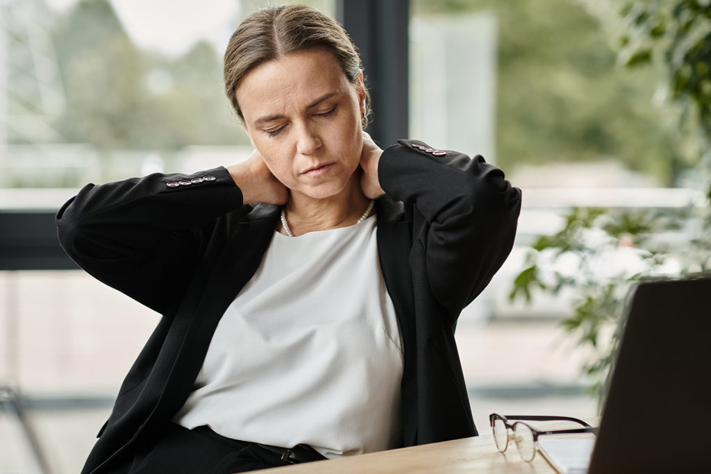 DojrzaÅa kobieta masujÄ
ca sobie kark i siedzÄ
ca za biurkiem
